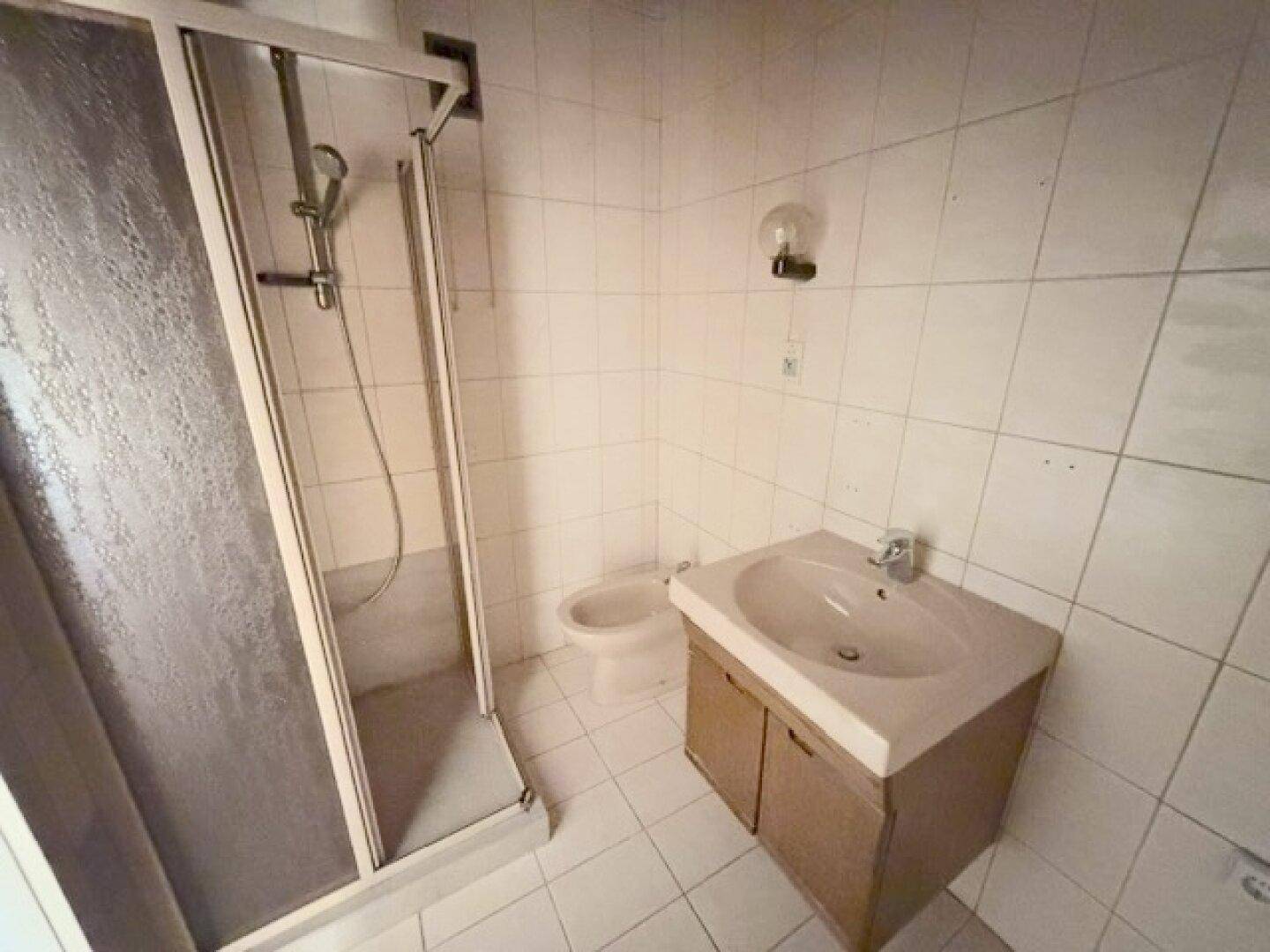 Helles Badezimmer mit Duschkabine, Waschbecken und Bidet, vollständig gefliest, funktional und sauber.