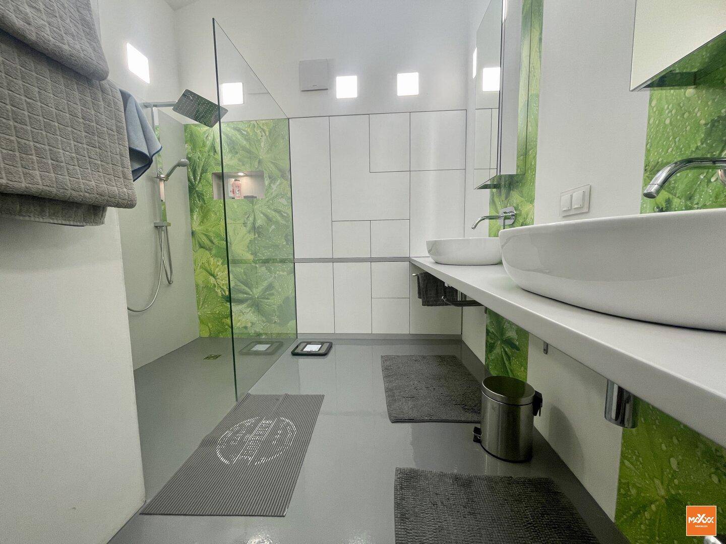 Modernes Badezimmer mit Doppelwaschbecken, begehbarer Dusche und grünen Akzenten.