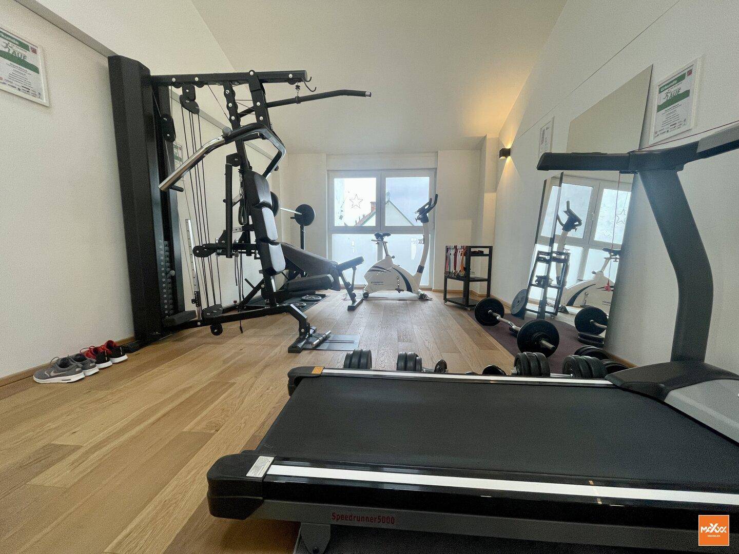 Privater Fitnessraum mit Laufband, Hanteln und Trainingsgeräten.