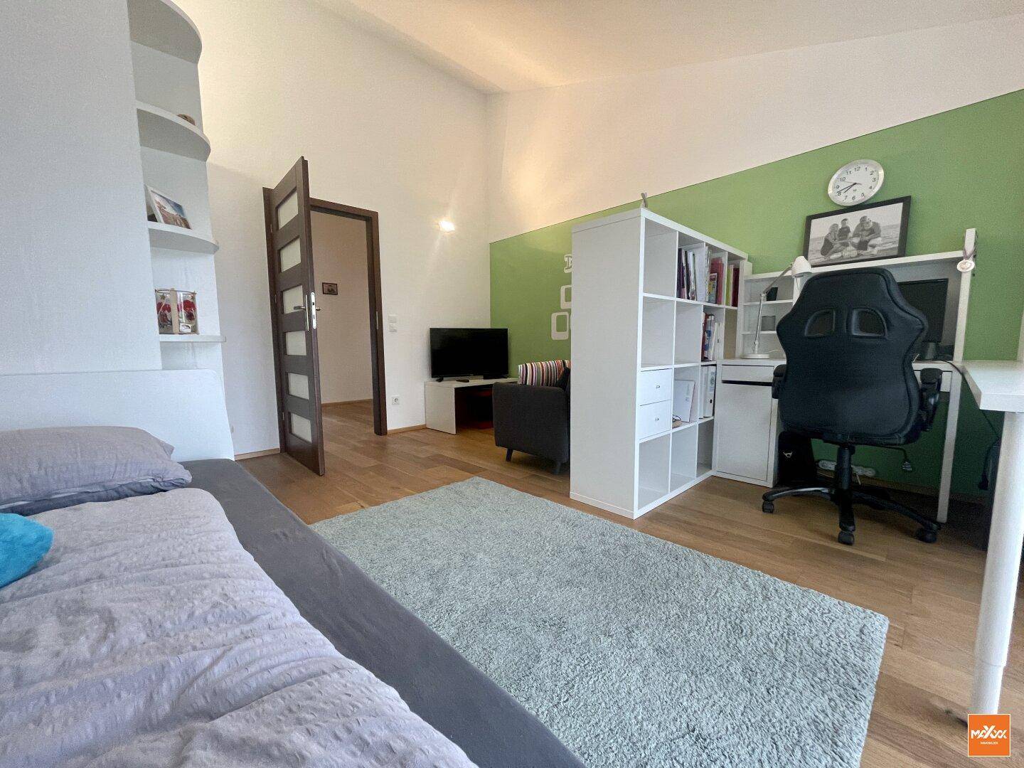 Helles Kinderzimmer mit Holzboden, Schreibtisch und grüner Akzentwand.