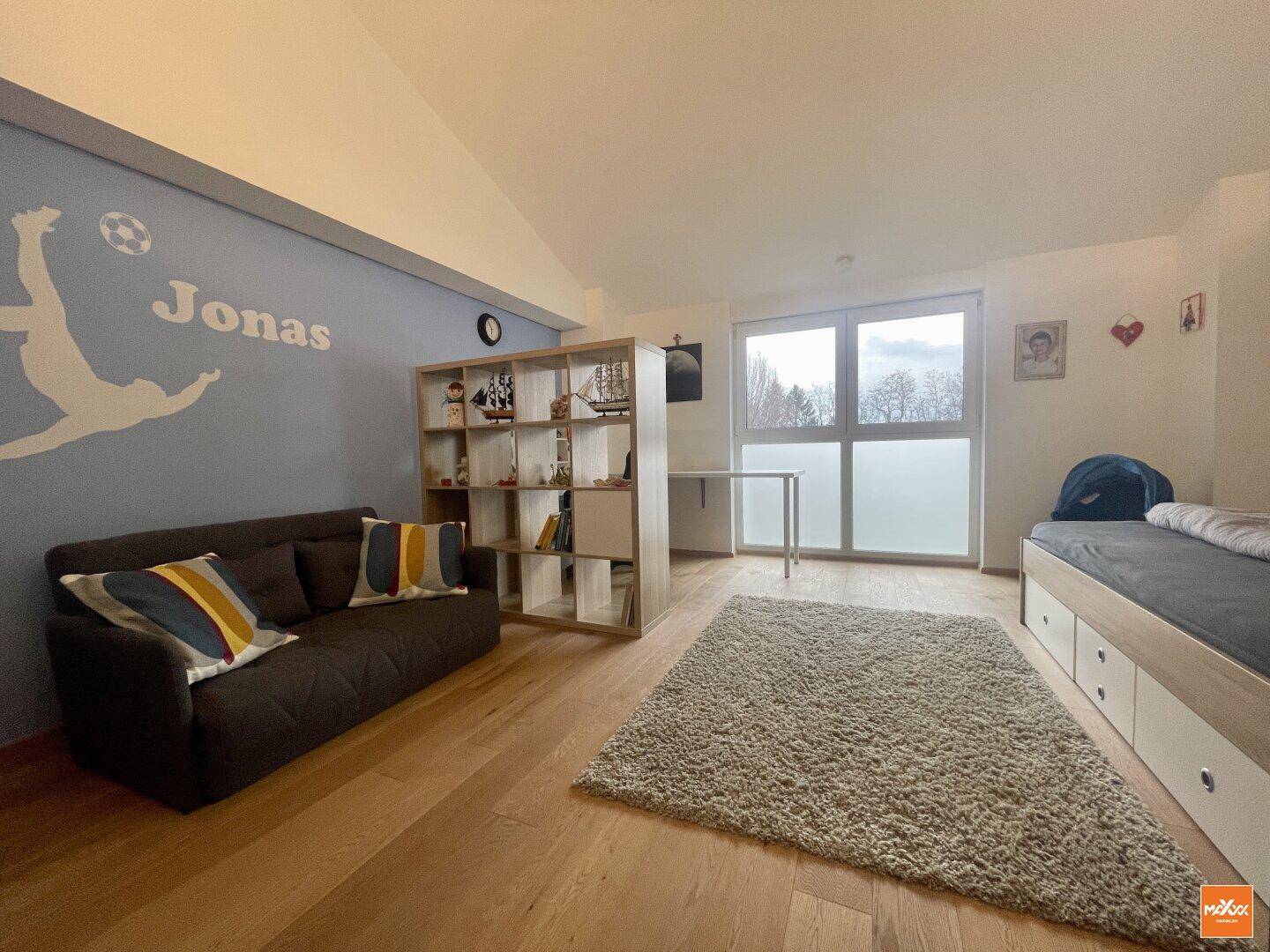 Kinderzimmer mit Holzboden, Sofa und großem Fenster für viel Tageslicht.