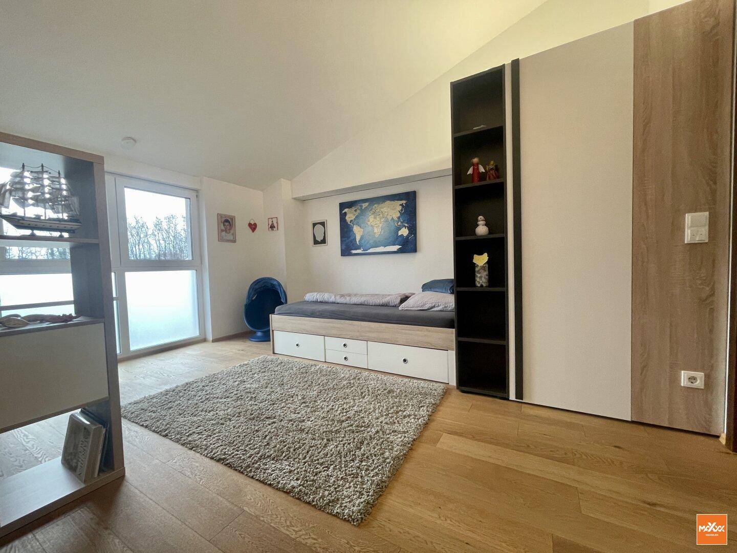 Kinderzimmer mit Holzboden, Bett und Schrankwand mit integrierten Regalen.