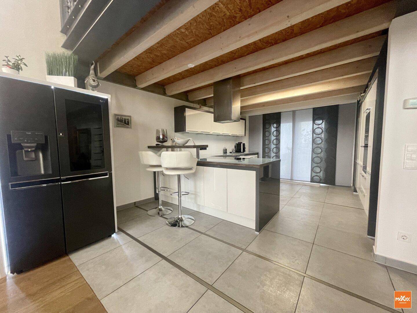 Moderne Küche mit Kücheninsel, Barhockern und großem Kühlschrank in offenem Wohnbereich.