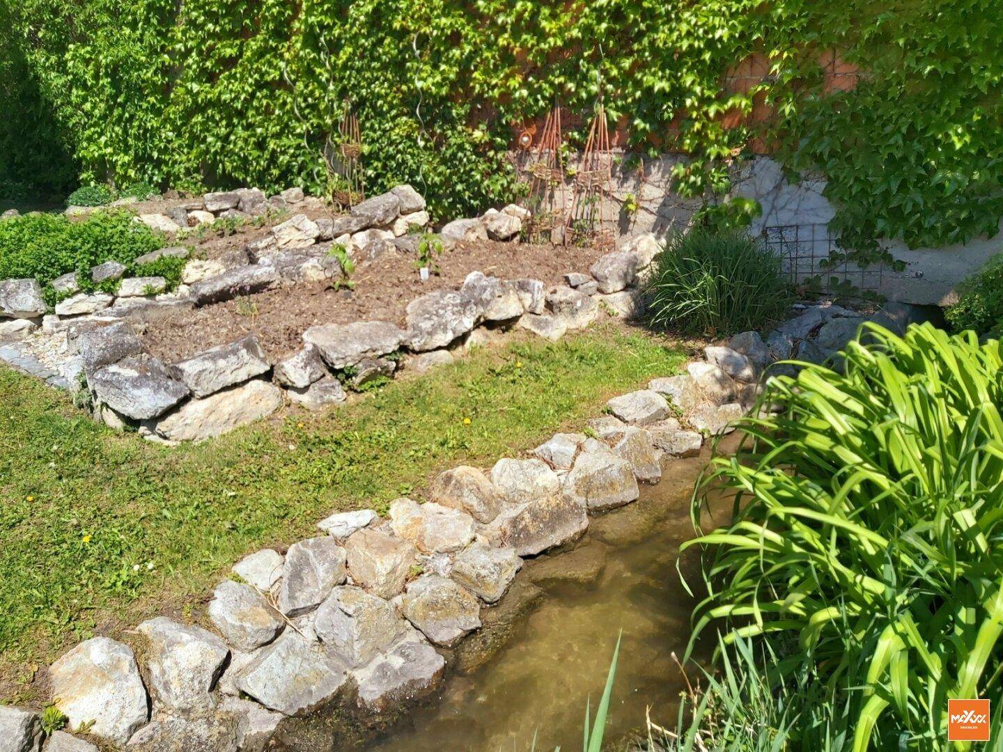 Mediterraner Steingarten mit Bachlauf und üppiger Bepflanzung.