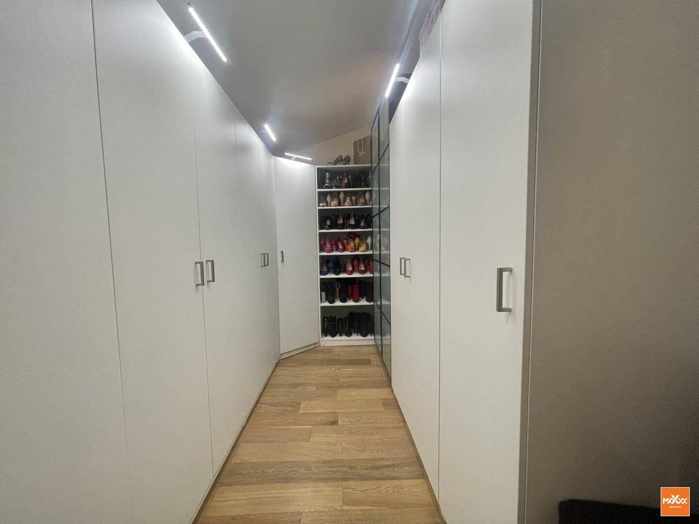 Geräumiger begehbarer Kleiderschrank mit viel Stauraum und integrierter Beleuchtung.