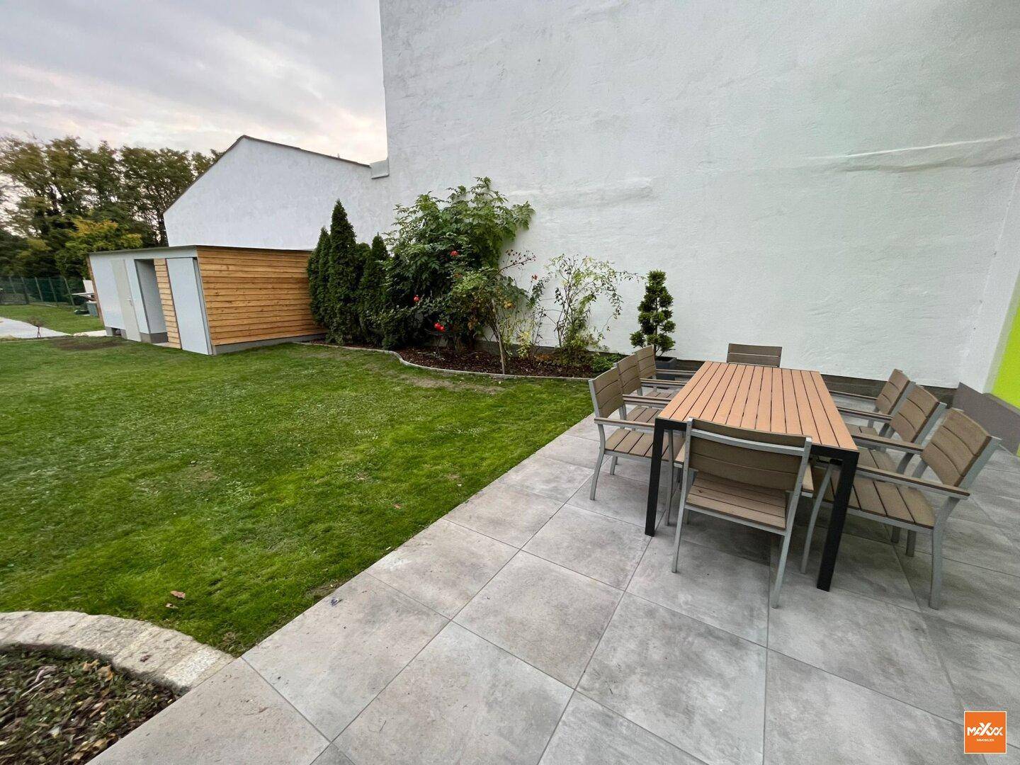 Gemütliche Terrasse mit Gartenmöbeln, Fliesenboden und Blick auf den Rasen.