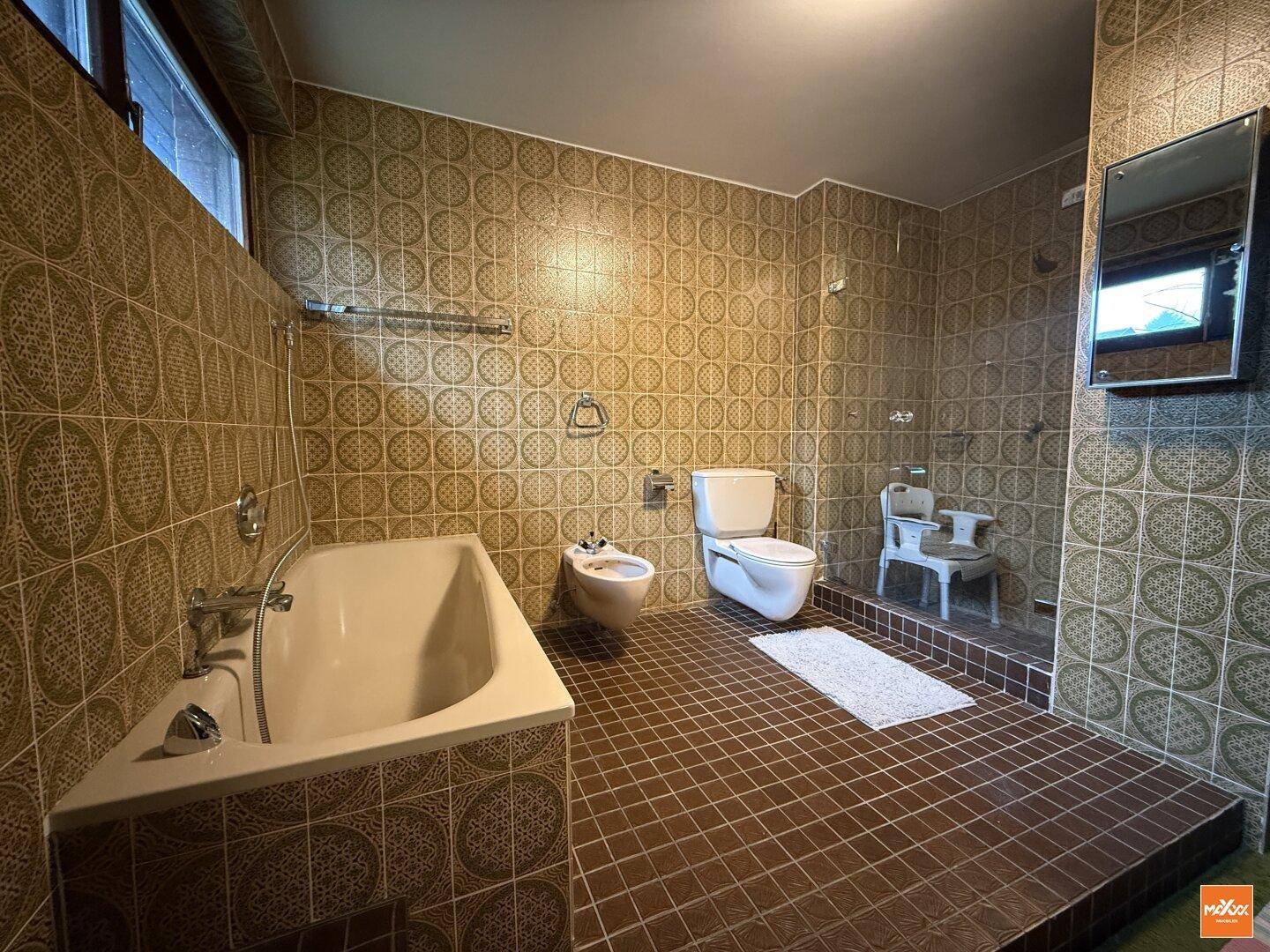 Badezimmer im 80er-Jahre-Stil mit braunen Fliesen, Badewanne, Bidet und Toilette.