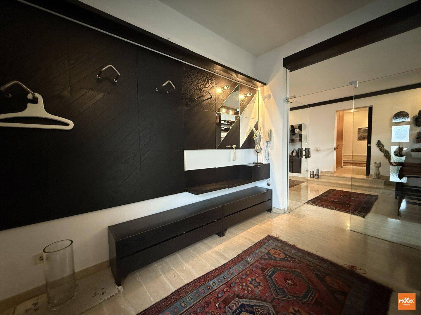 Heller Eingangsbereich mit dunkler Garderobe, Spiegeln und gemustertem Teppich auf Marmorboden.