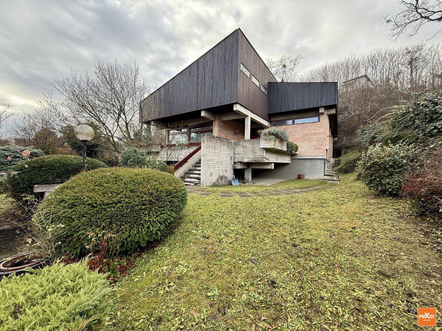 Ansicht des modernen Hauses von der Gartenseite mit Treppen und umgebender Vegetation.