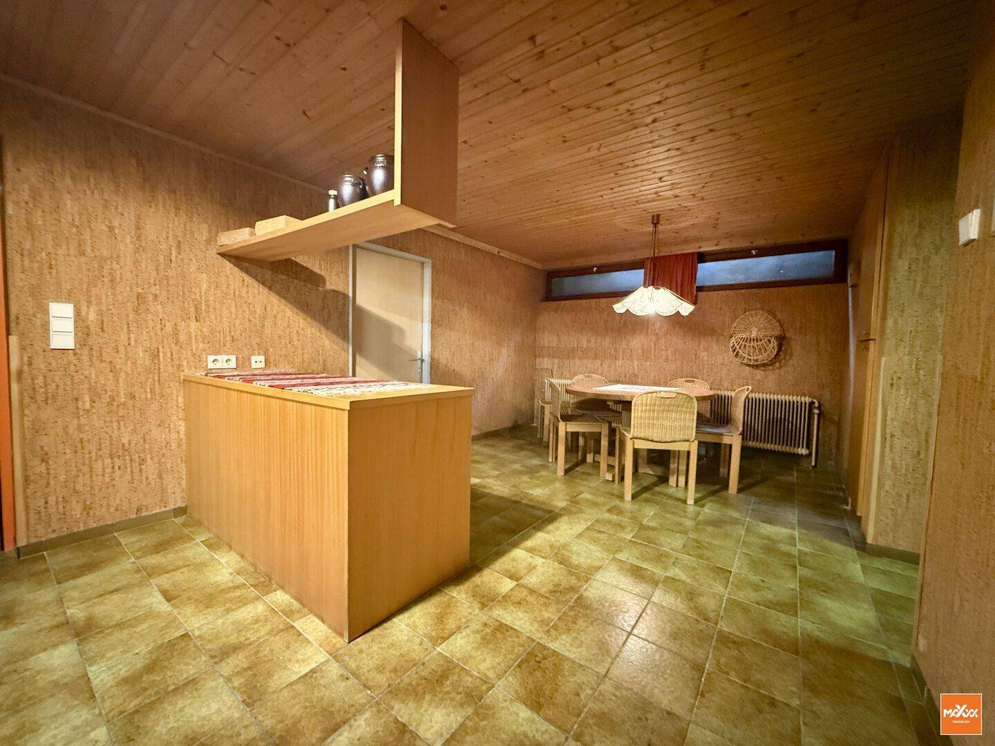 Rustikaler Raum im Untergeschoss mit Holzwänden, Fliesenboden und Essbereich.