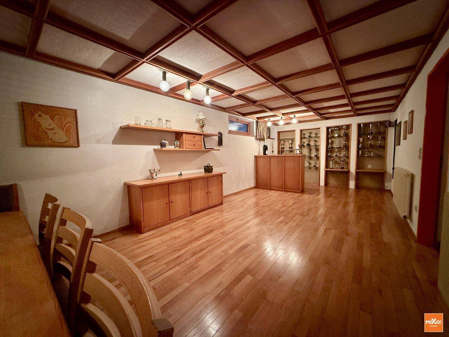 Großer Hobbyraum im Untergeschoss mit Holzparkett, Deckenpaneelen und Vitrinen.