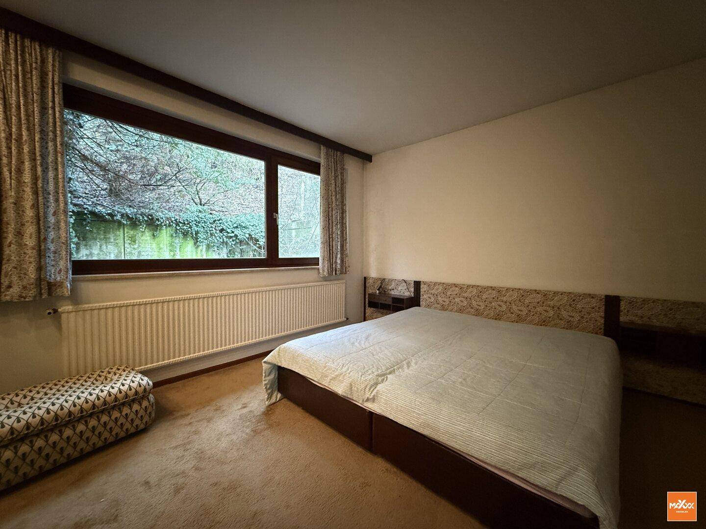 Schlafzimmer mit Doppelbett, Teppichboden und großem Fenster mit Blick auf die umgebende Natur.