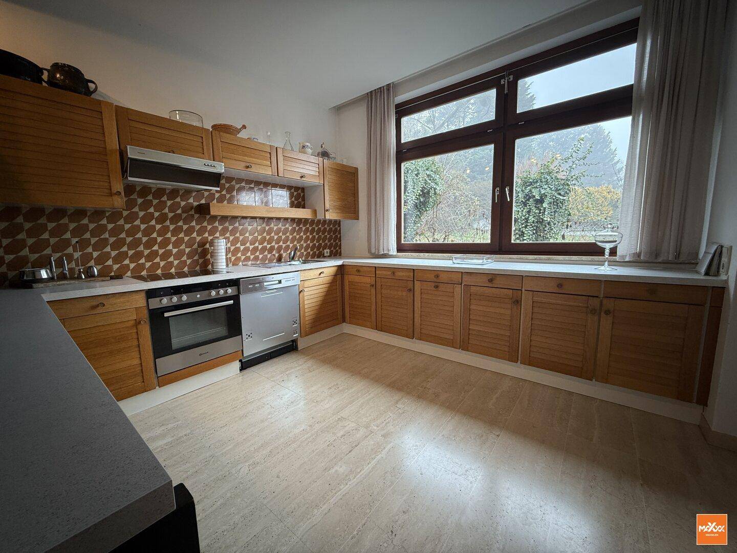 Geräumige Küche im Vintage-Stil mit Holzschränken, gemusterten Fliesen und großem Fenster zum Garten.