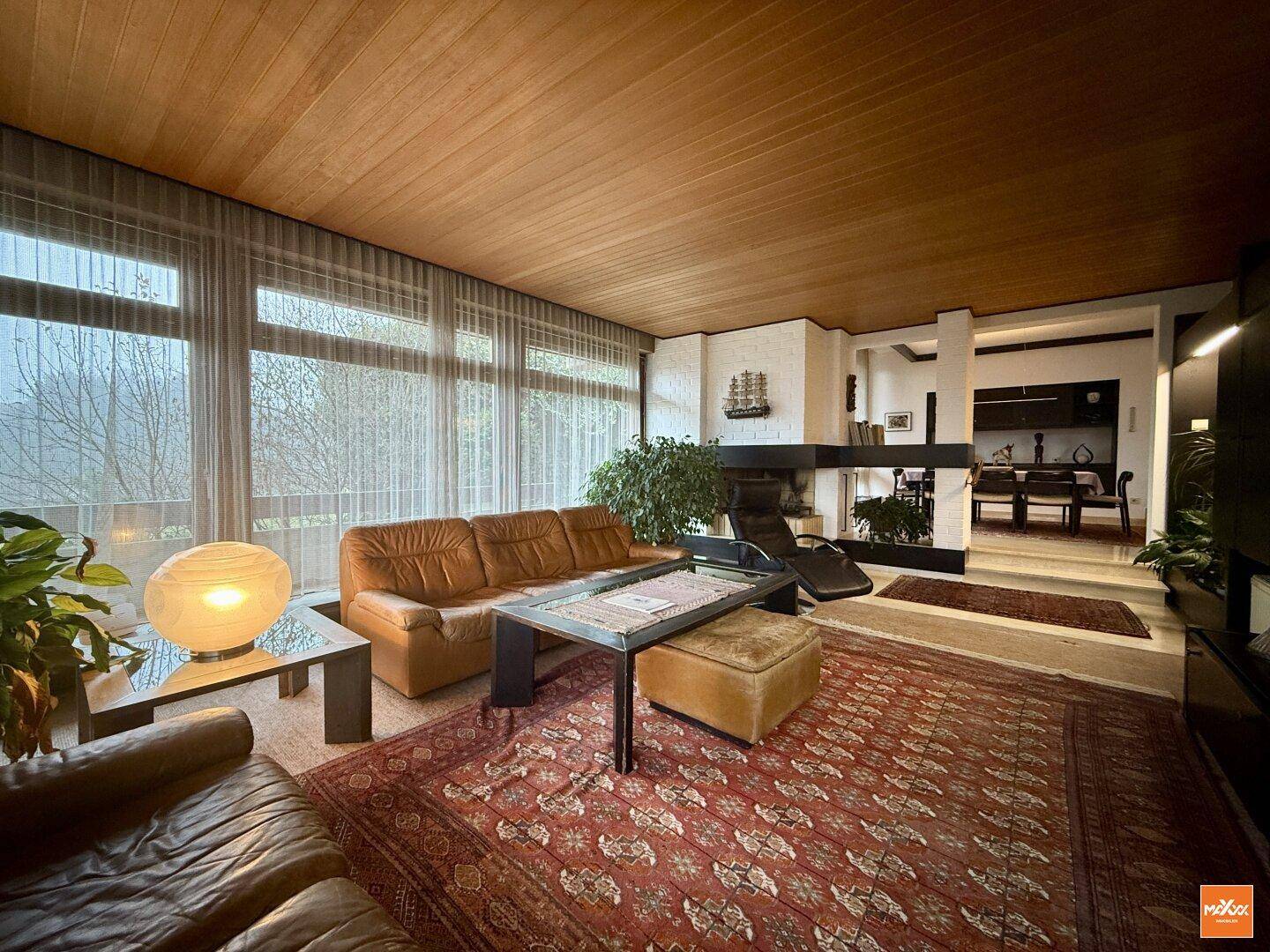 Gemütliches Wohnzimmer mit Ledersofas, Holztäfelung an der Decke und großen Fenstern mit Blick ins Grüne.