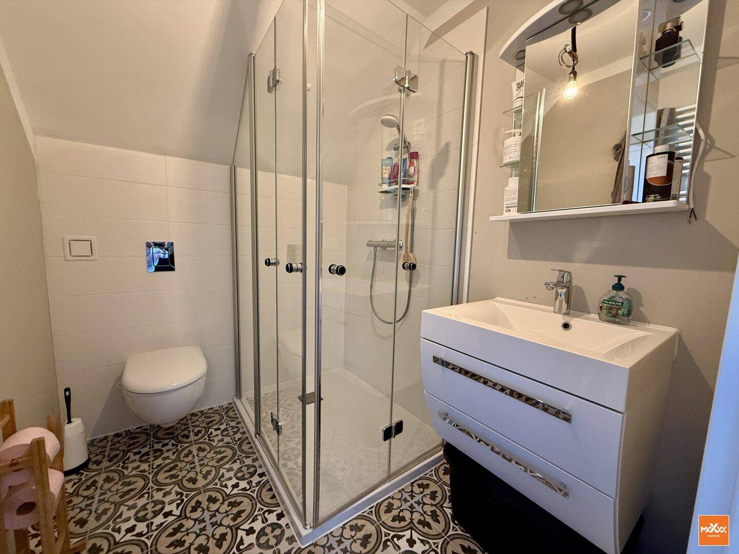 Modernes Badezimmer im Dachgeschoss mit Dusche, WC und gemusterten Bodenfliesen.