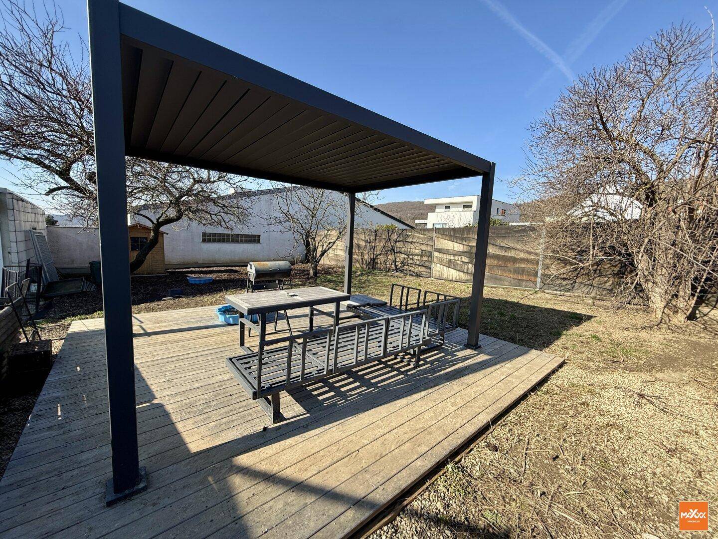 Große Holzterrasse mit Pergola, Essbereich im Freien und Blick ins Grüne.