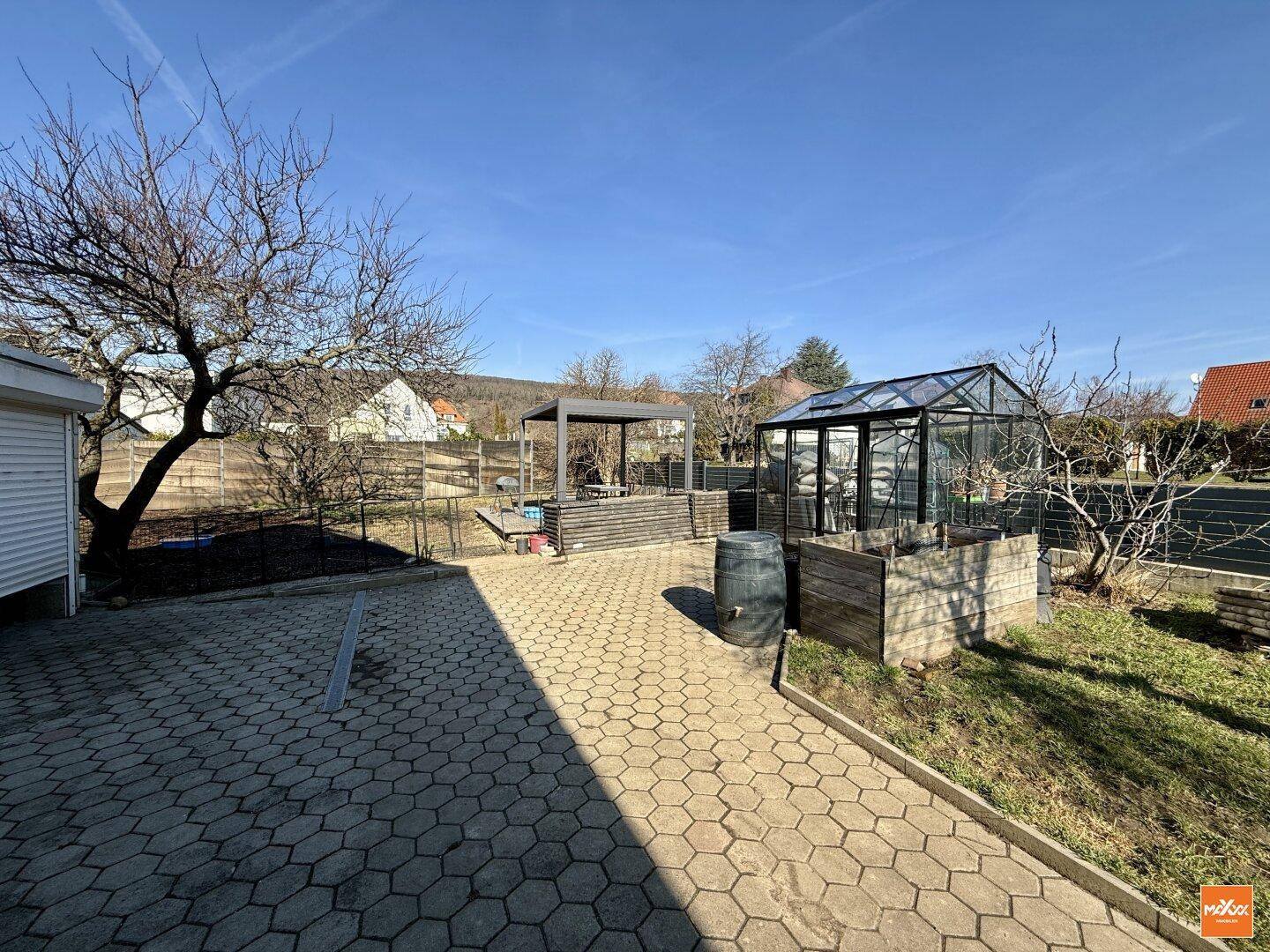 Gepflasterter Gartenbereich mit Gewächshaus, Hochbeeten und viel Platz im Freien.