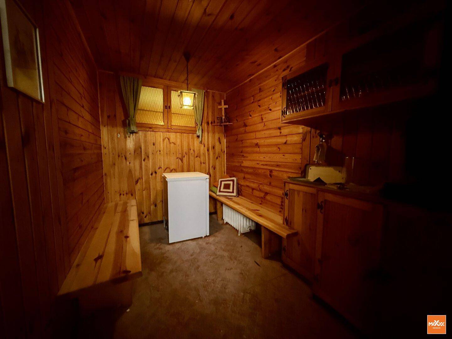 Rustikaler Kellerraum mit Holzvertäfelung, Sitzbänken und kleinem Kühlschrank.