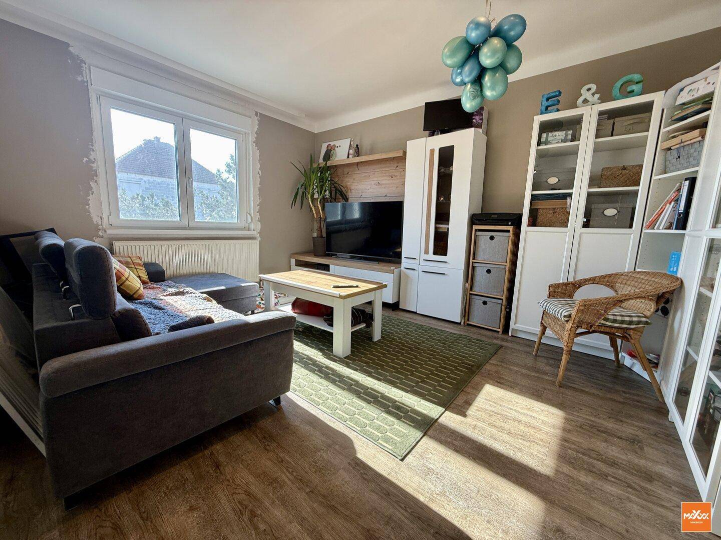 Helles Wohnzimmer mit Laminatboden, großem Fenster und moderner Einrichtung.