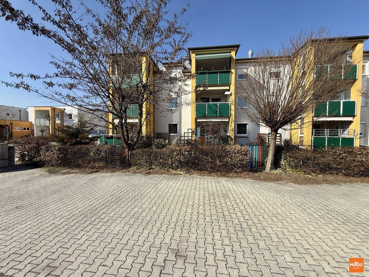 Mehrfamilienhaus mit gelb-weißer Fassade, Balkonen und Außenparkplätzen.