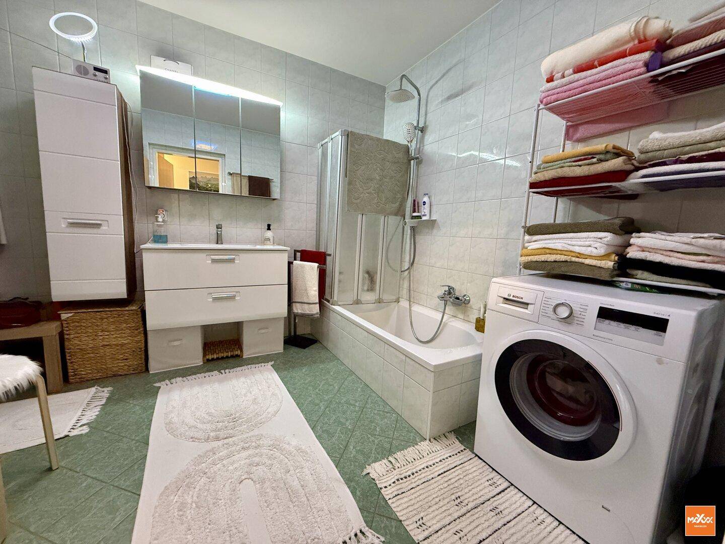 Funktionales Badezimmer mit Badewanne, Duschbereich, Waschbecken und Waschmaschine.