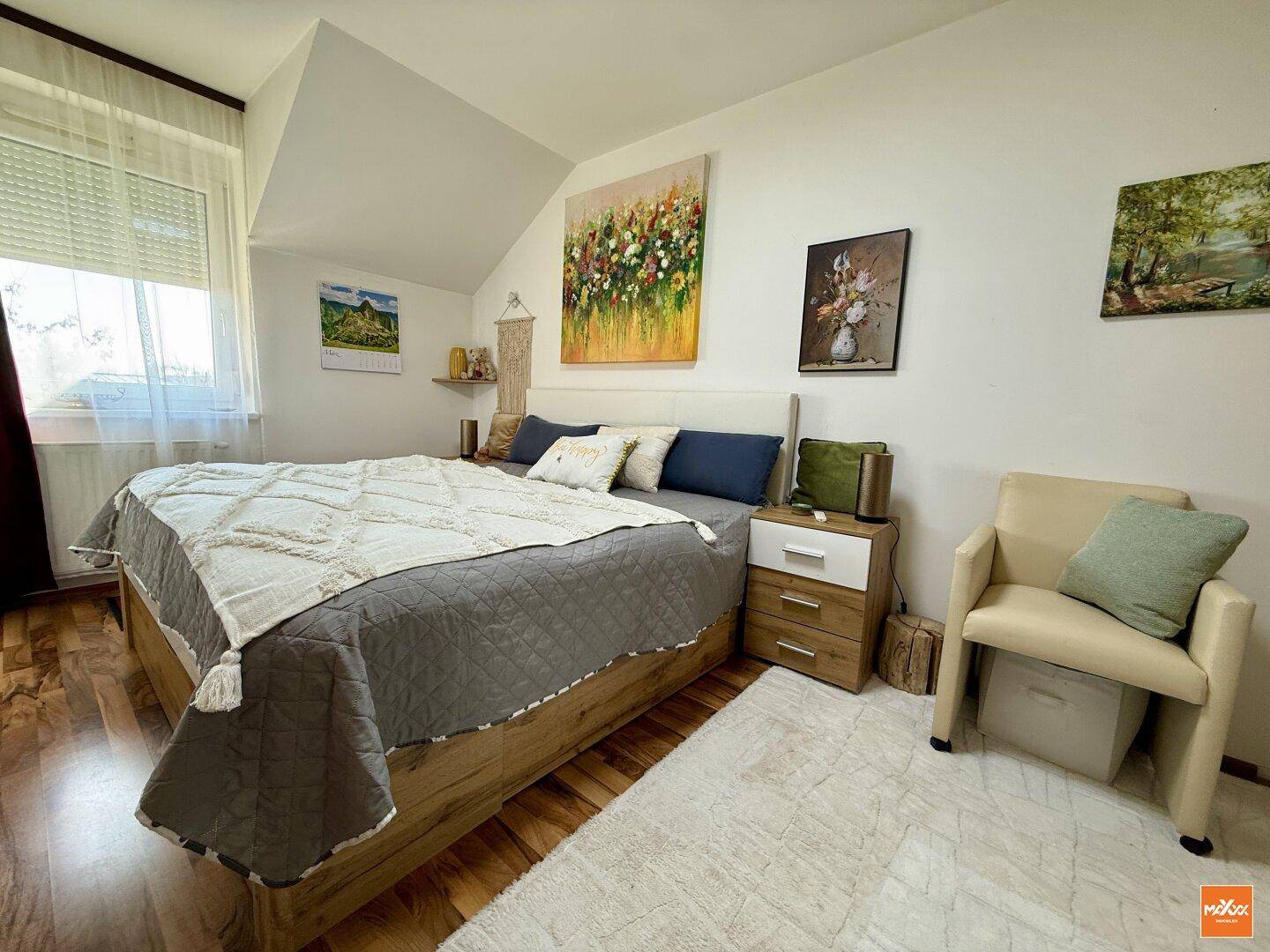 Helles Schlafzimmer mit Holzboden, großem Bett und schräger Decke.