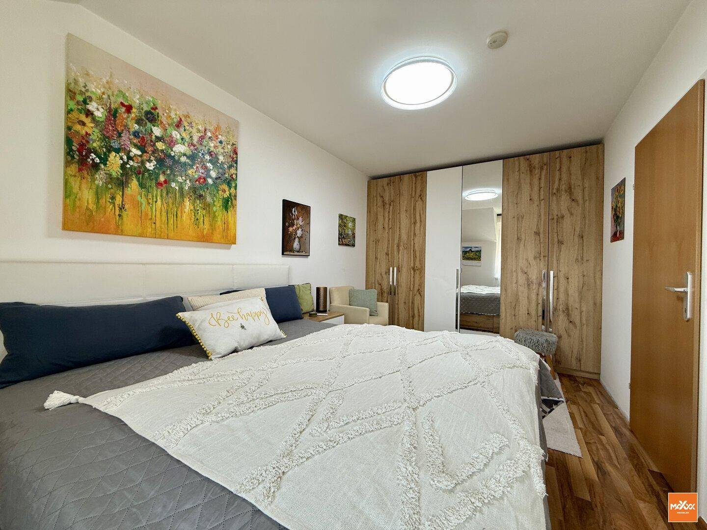 Schlafzimmer mit geräumigem Kleiderschrank, Spiegeltüren und Holzboden.