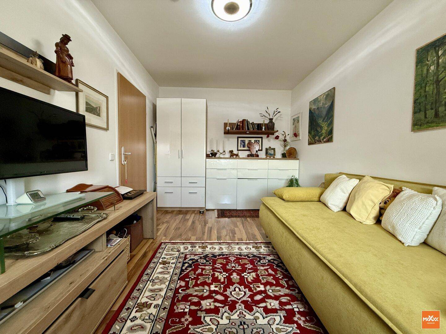 Gemütliches Zimmer mit Sofa, Fernseher und praktischen weißen Schränken.