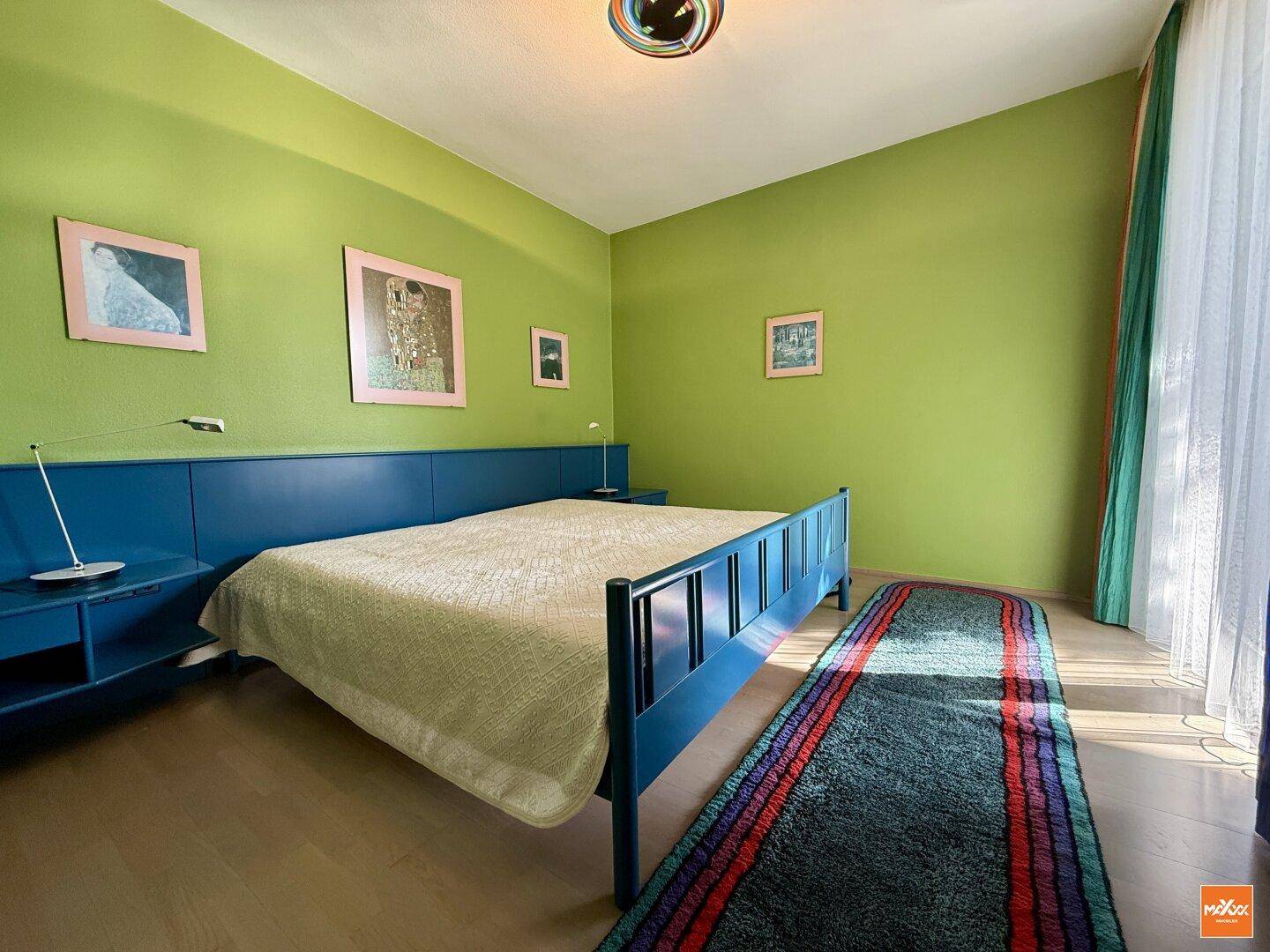 Schlafzimmer mit leuchtend grünen Wänden, blauem Bettrahmen und Holzboden.