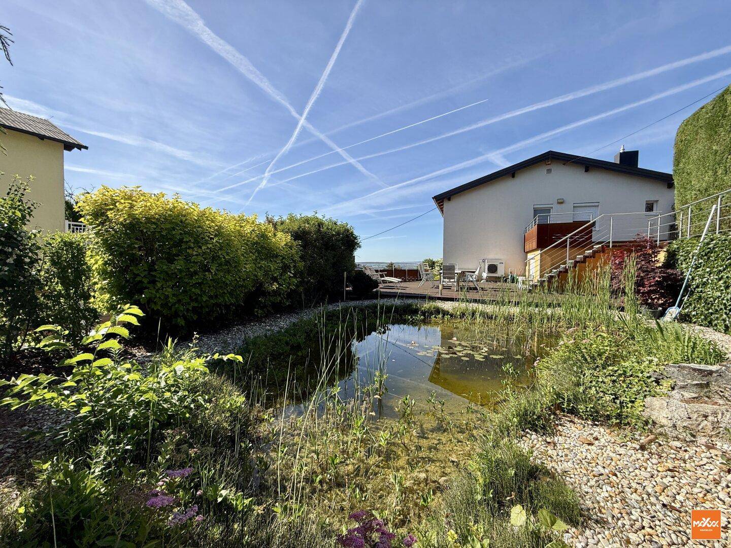 Gartenbereich mit einem Teich und einer Holzterrasse im Hintergrund, die zum Haus gehört.