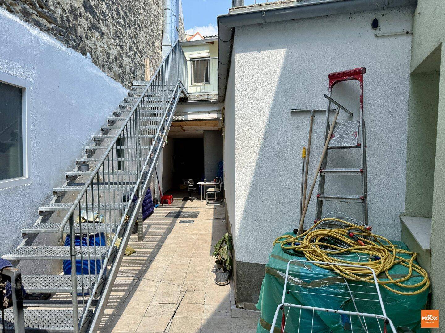 Außenbereich mit Metalltreppe und gefliestem Weg, der zu weiteren Gebäudeteilen führt.