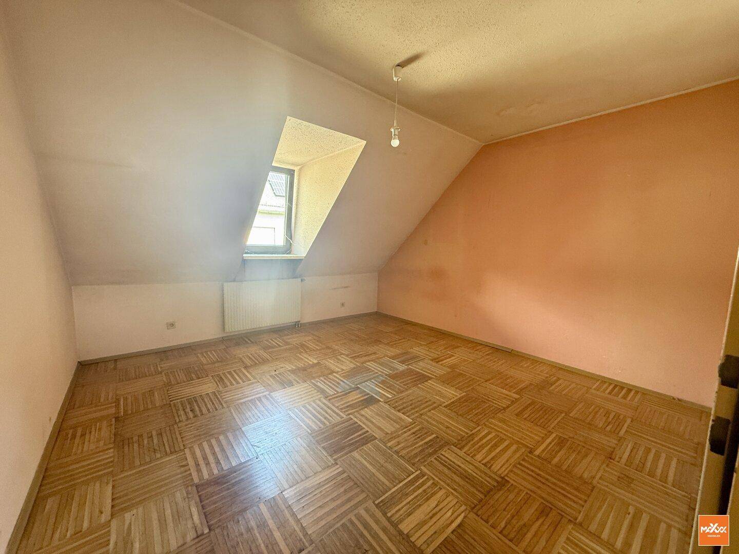 Schlafzimmer mit Dachschräge, Parkettboden und einem kleinen Fenster, bereit zur individuellen Gestaltung.