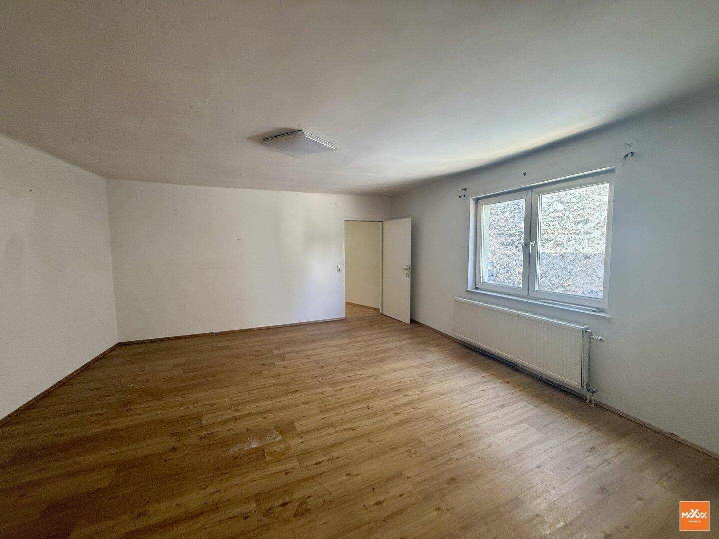 Geräumiges Wohnzimmer mit Holzboden und großem Fenster, das viel natürliches Licht bietet.