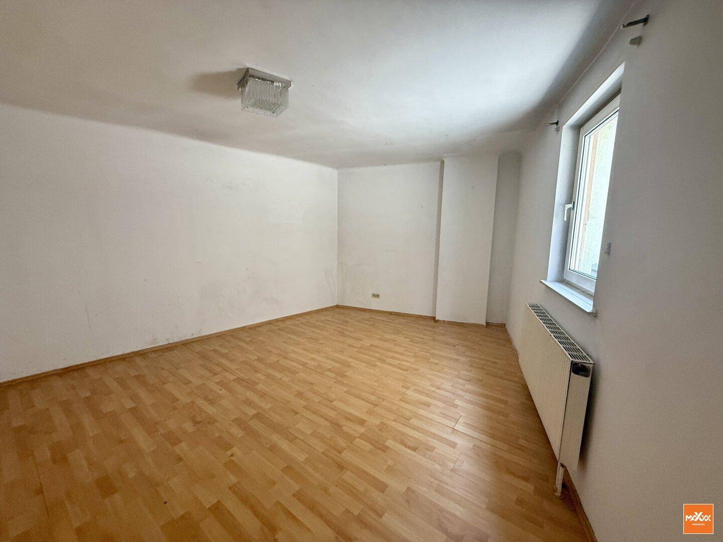 Helles Wohnzimmer mit Holzboden und einem großen Fenster, das den Raum gut belichtet.