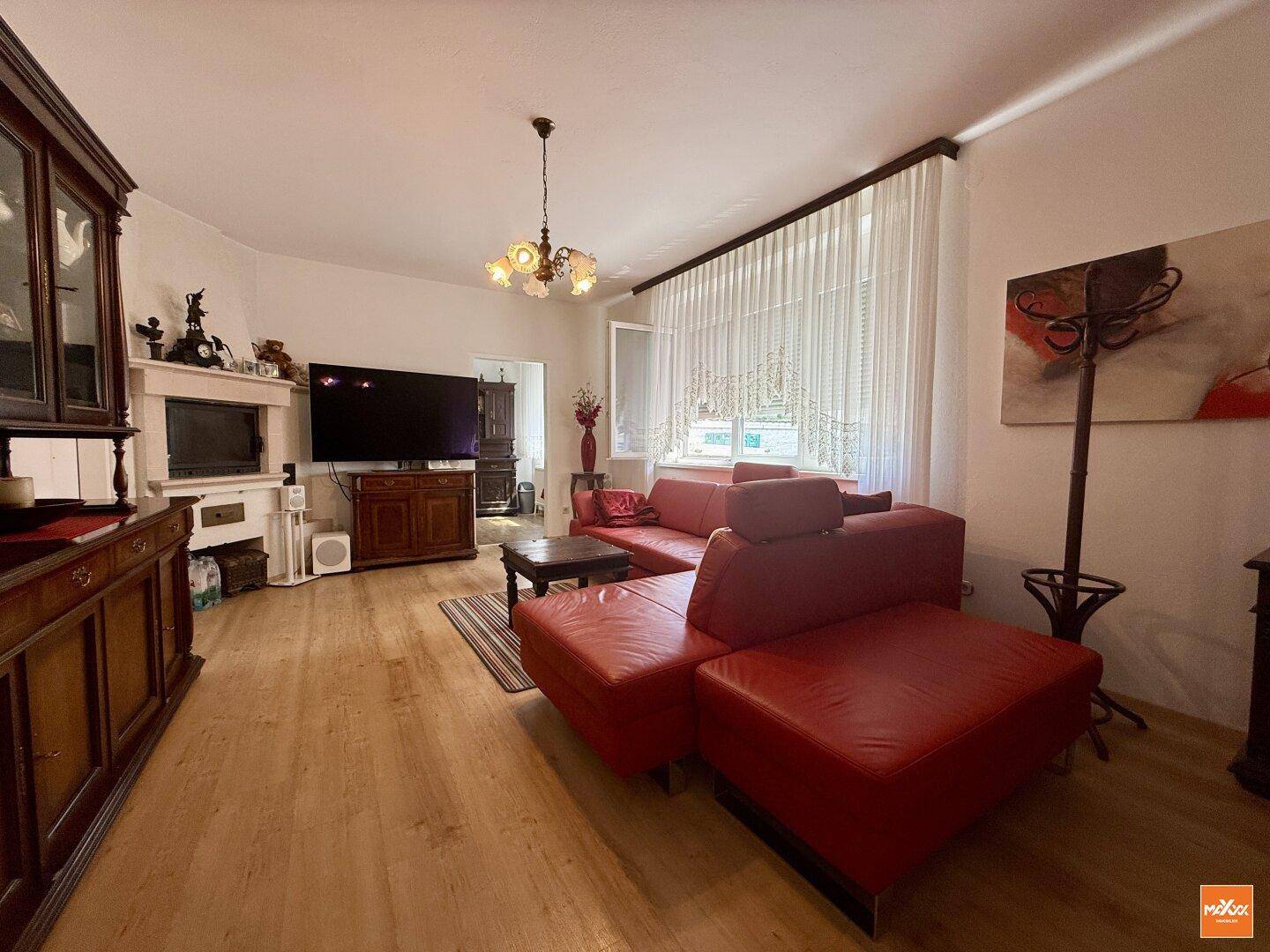Helles Wohnzimmer mit rotem Ledersofa, Holzboden und traditionellem Kronleuchter.