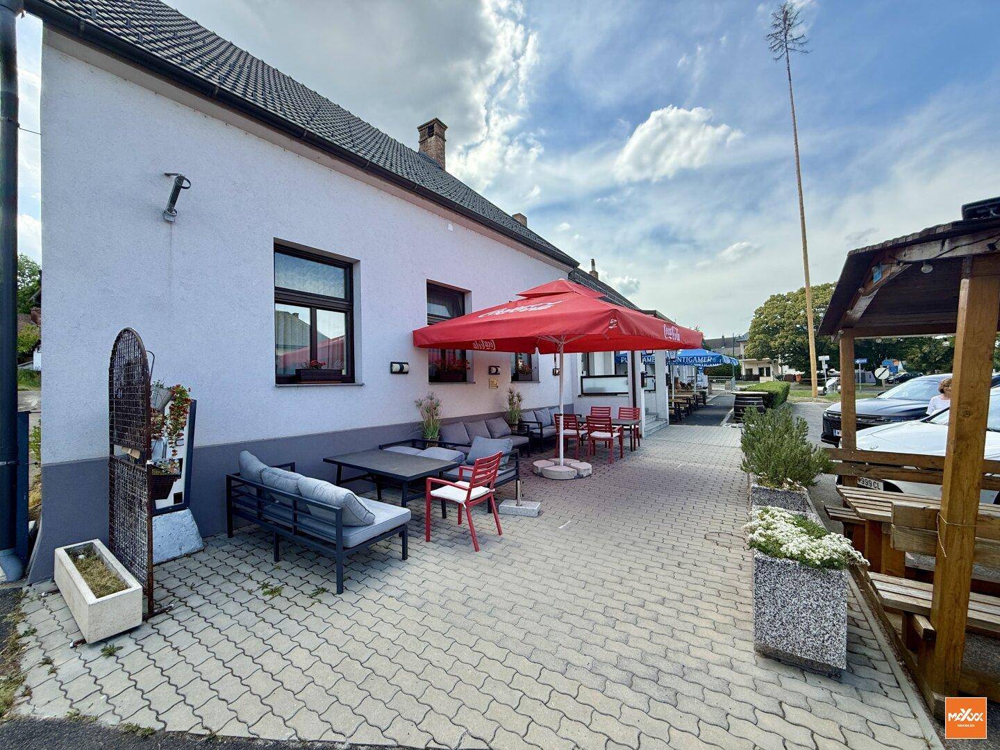 Gemütlicher Außenbereich mit roten Sonnenschirmen und Sitzgelegenheiten auf gepflastertem Boden.