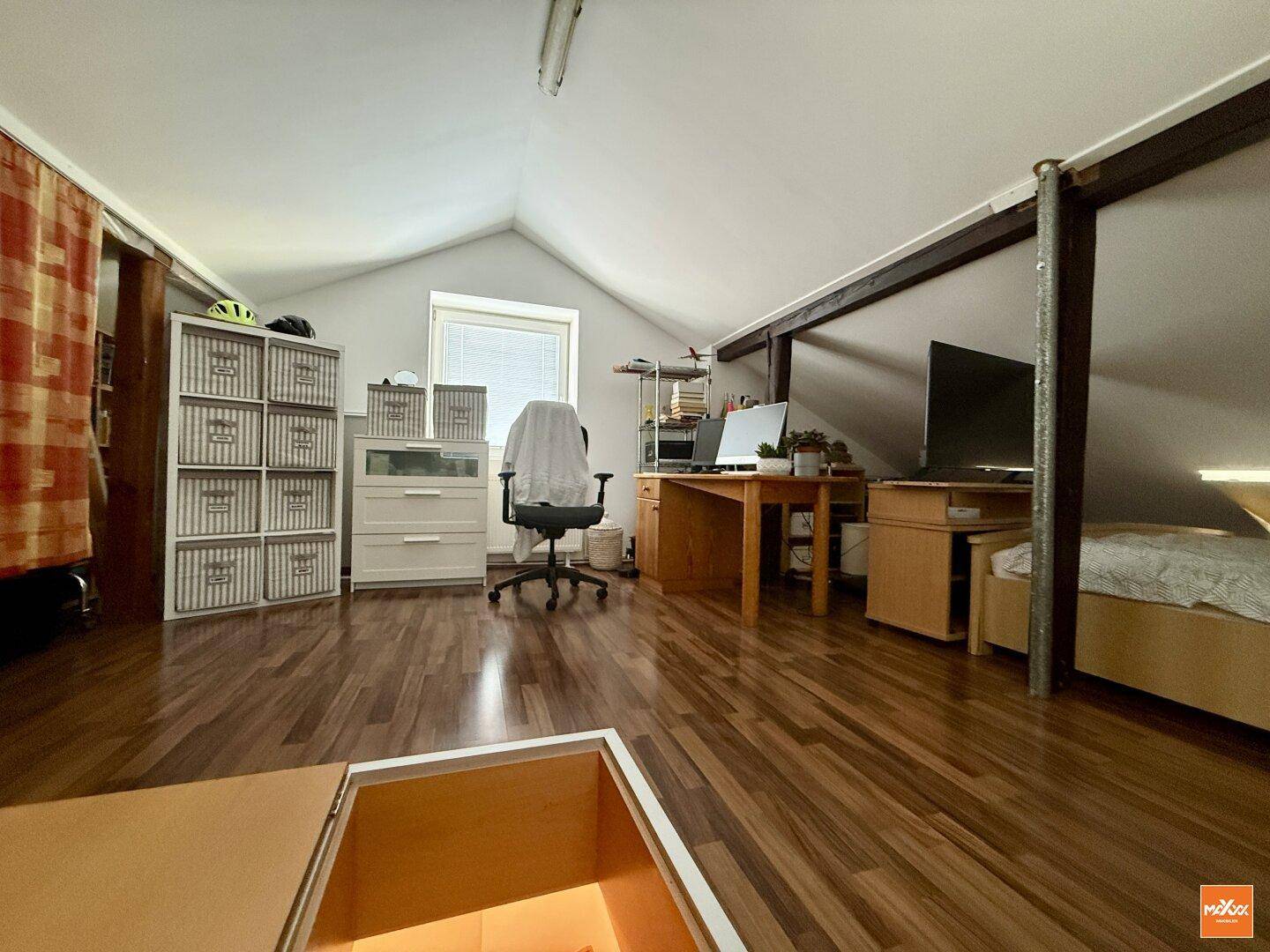 Dachzimmer mit Holzboden, Schreibtisch und schräger Decke.