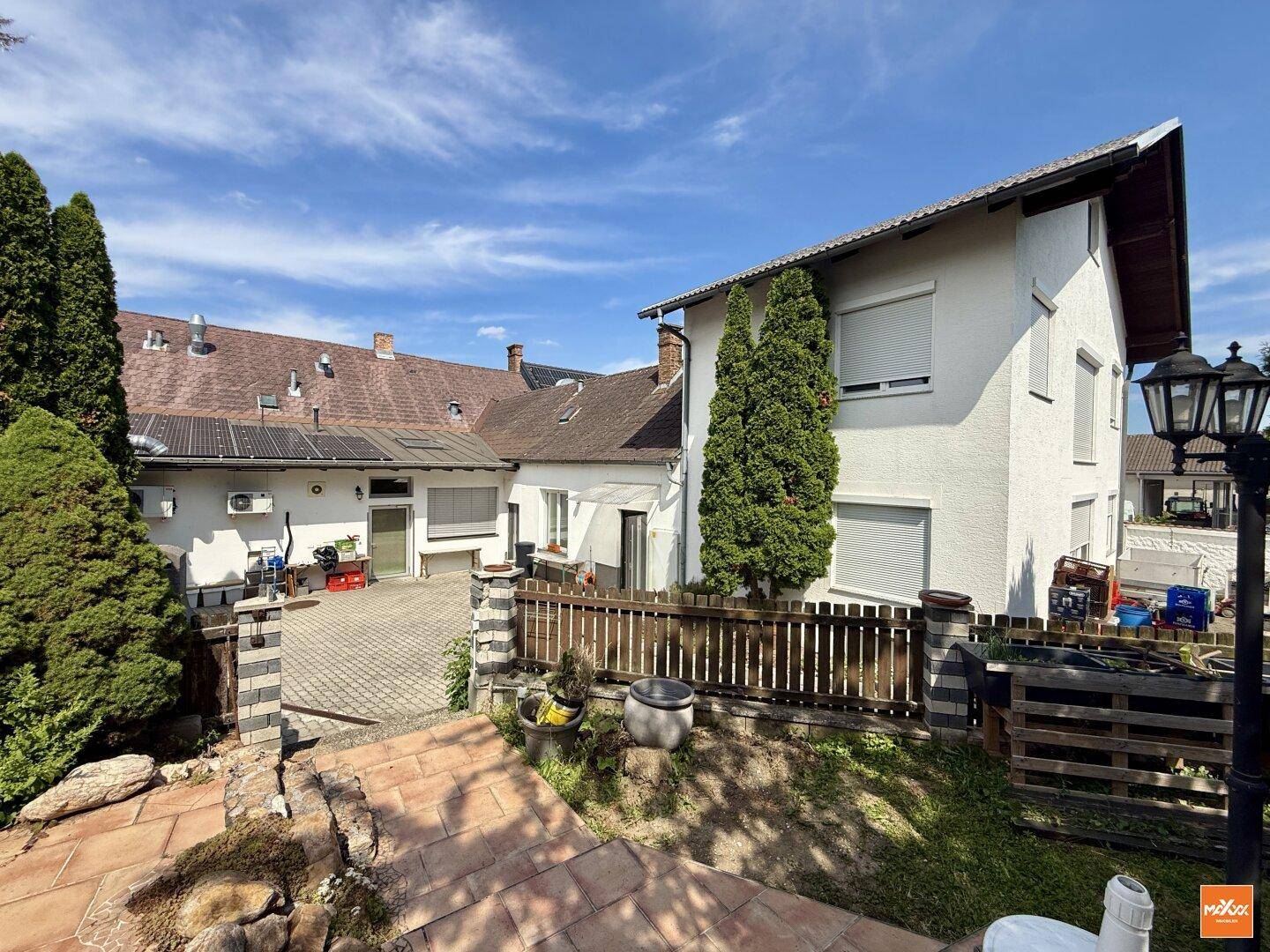 Hinterhofbereich mit Zaun, gepflastertem Weg und Solaranlage auf dem Dach.