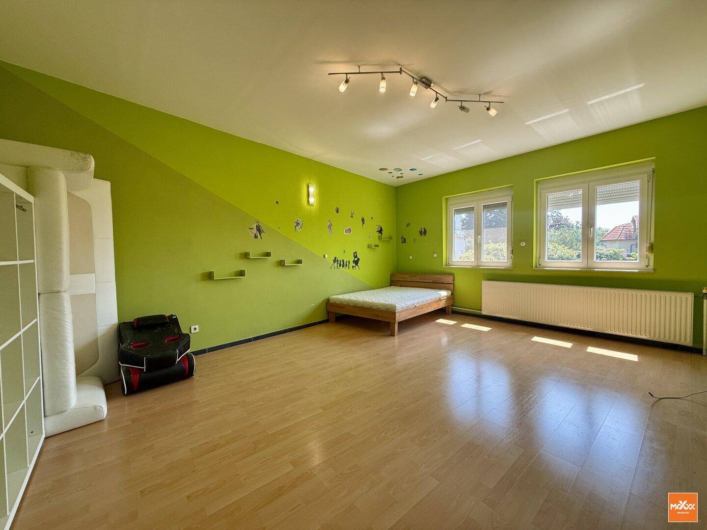 Kinderzimmer mit leuchtend grünen Wänden, Holzbett und Laminatboden.