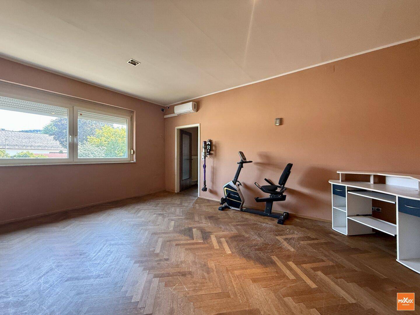 Helles Zimmer mit Fischgrätparkett, großem Fenster und Trainingsgerät.