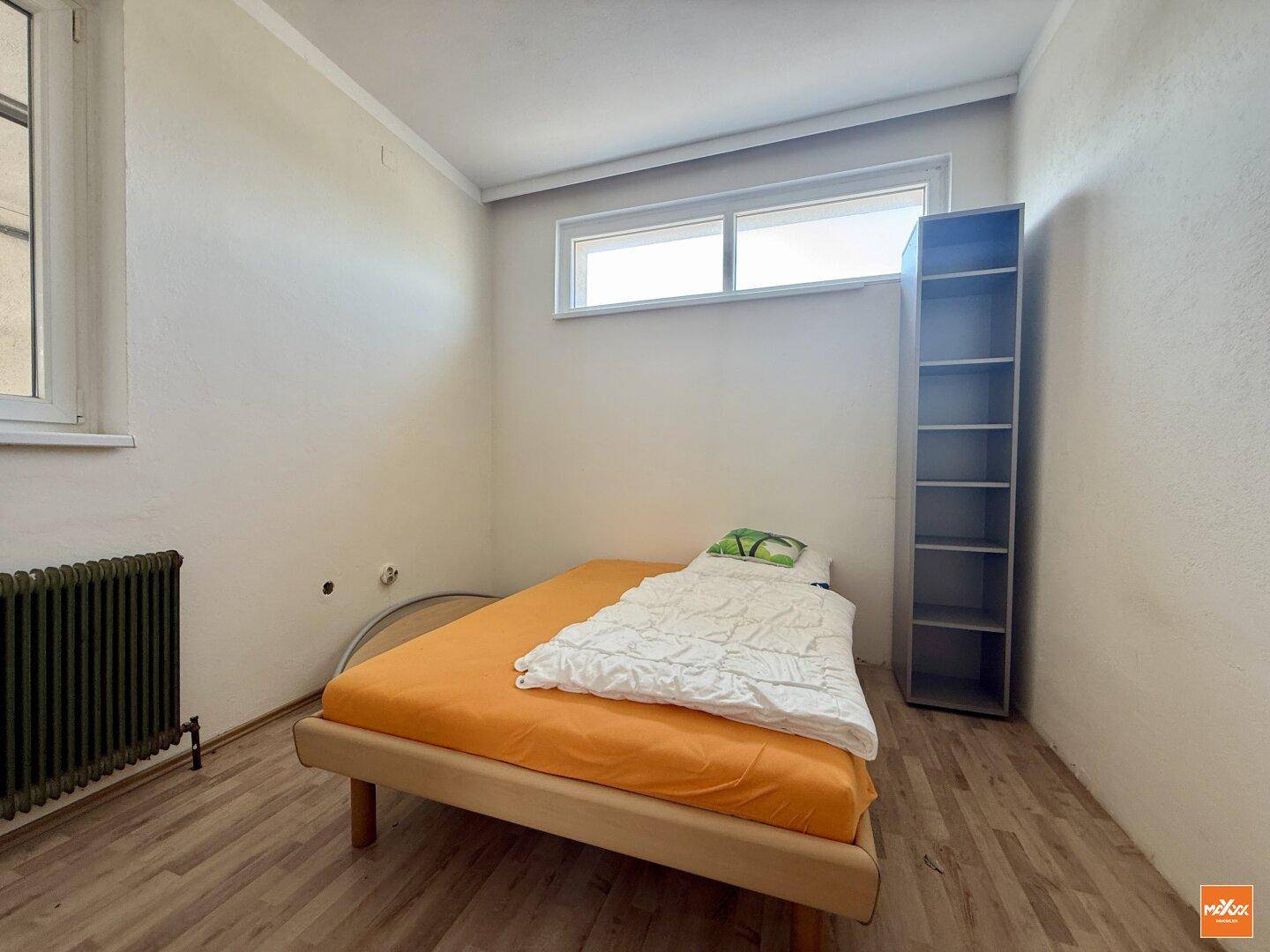 Schlafzimmer mit Einzelbett, Laminatboden und Fenster.