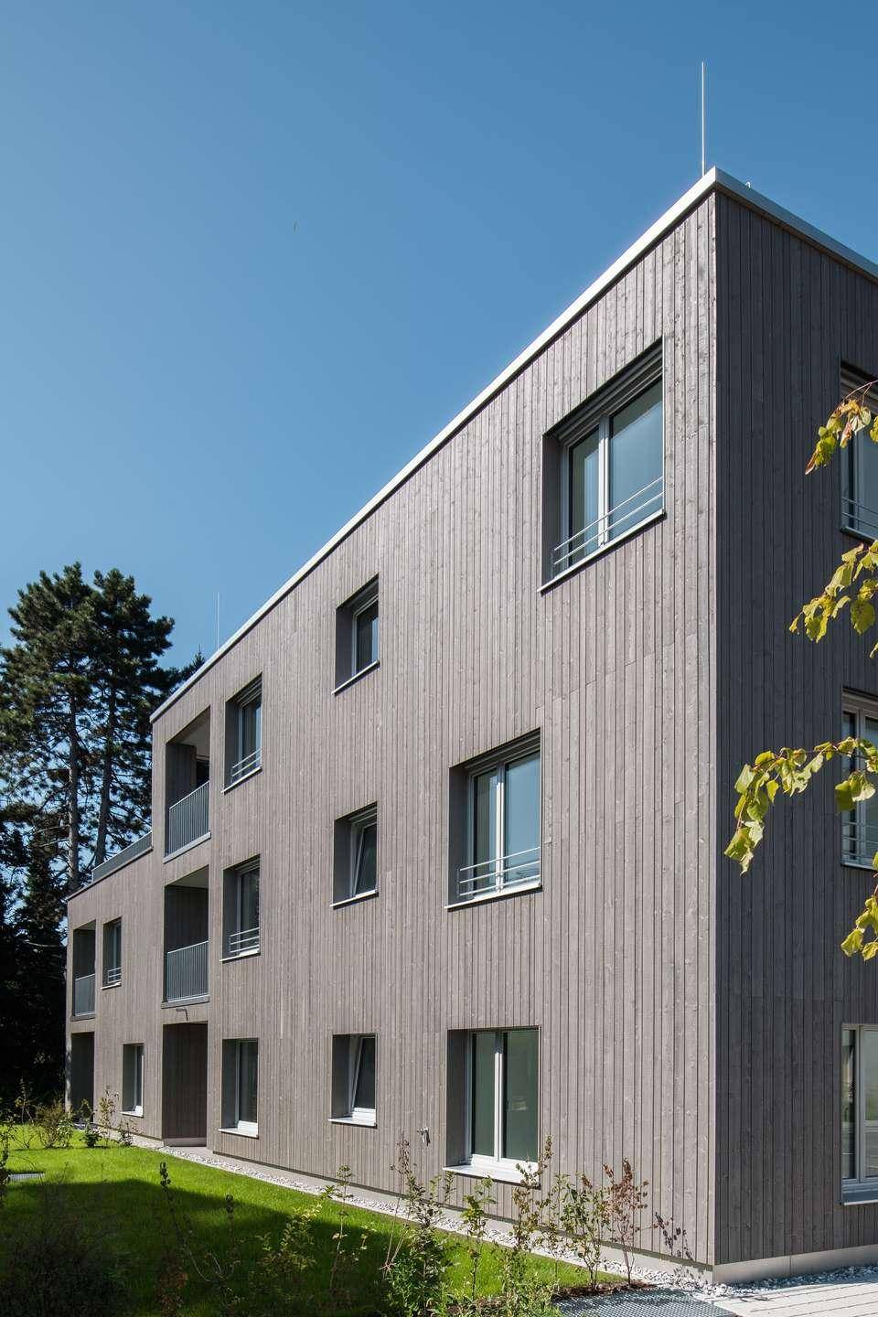 Eckansicht eines modernen Gebäudes mit vertikaler Holzfassade und großen Fenstern.