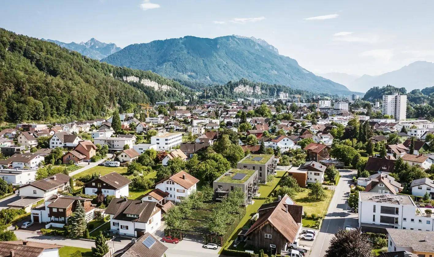Luftaufnahme einer Wohnsiedlung in einer malerischen Berglandschaft mit vielen Häusern und grünen Dächern.