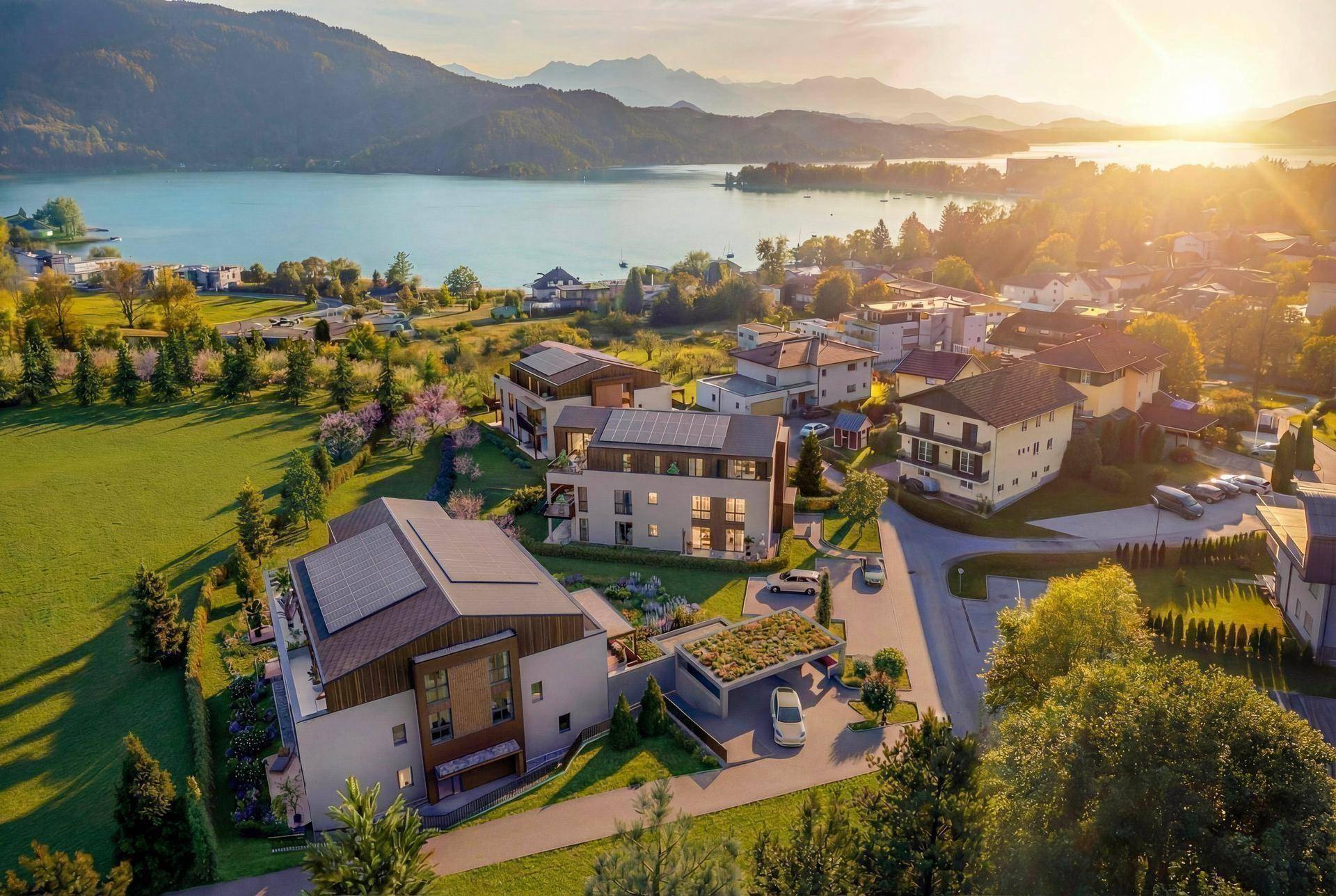 Luftaufnahme einer modernen Wohnanlage am Seeufer mit umliegender Natur und Bergpanorama bei Sonnenuntergang.