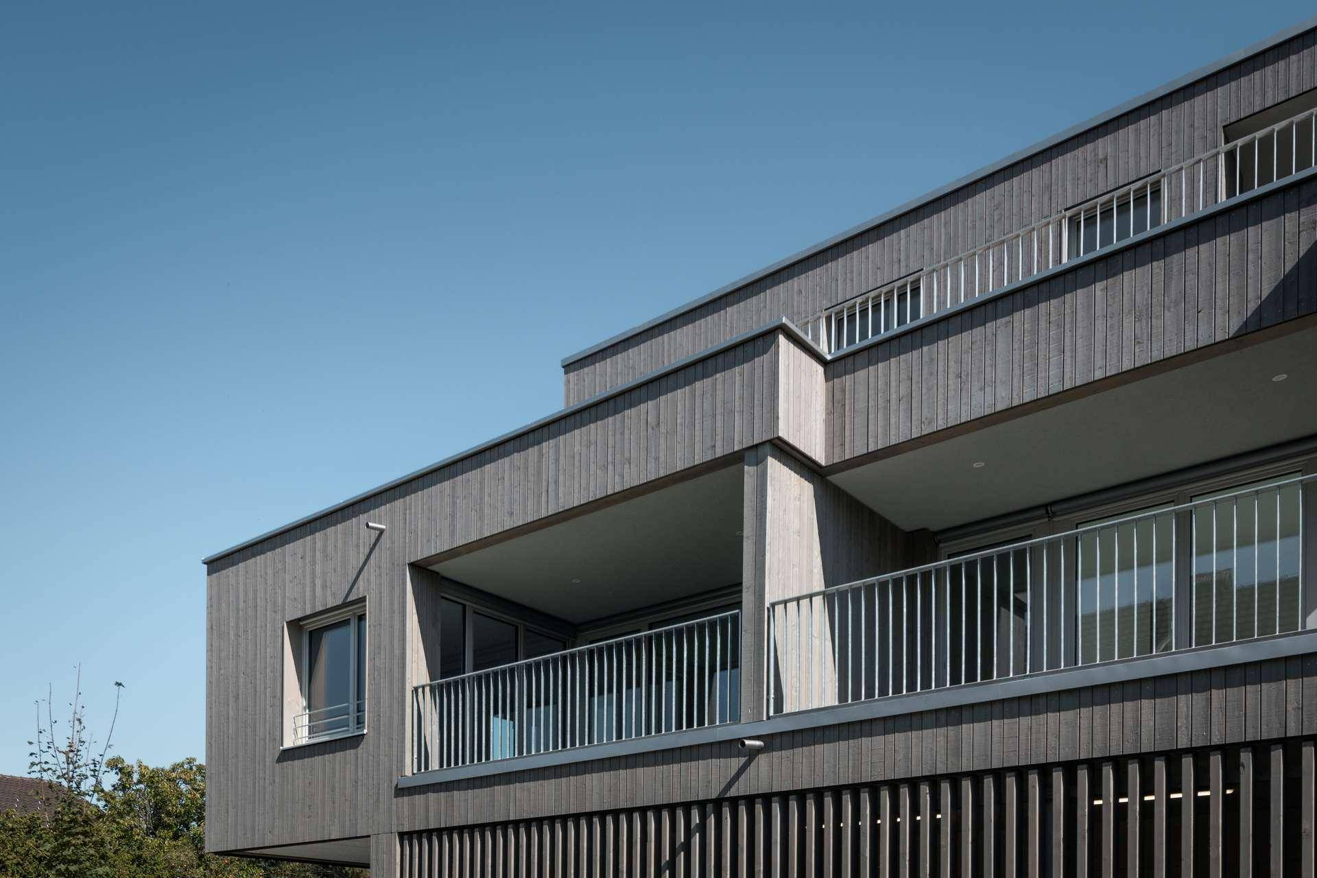 Detailansicht der modernen Holzfassade mit mehreren Balkonen und Metallgeländern.