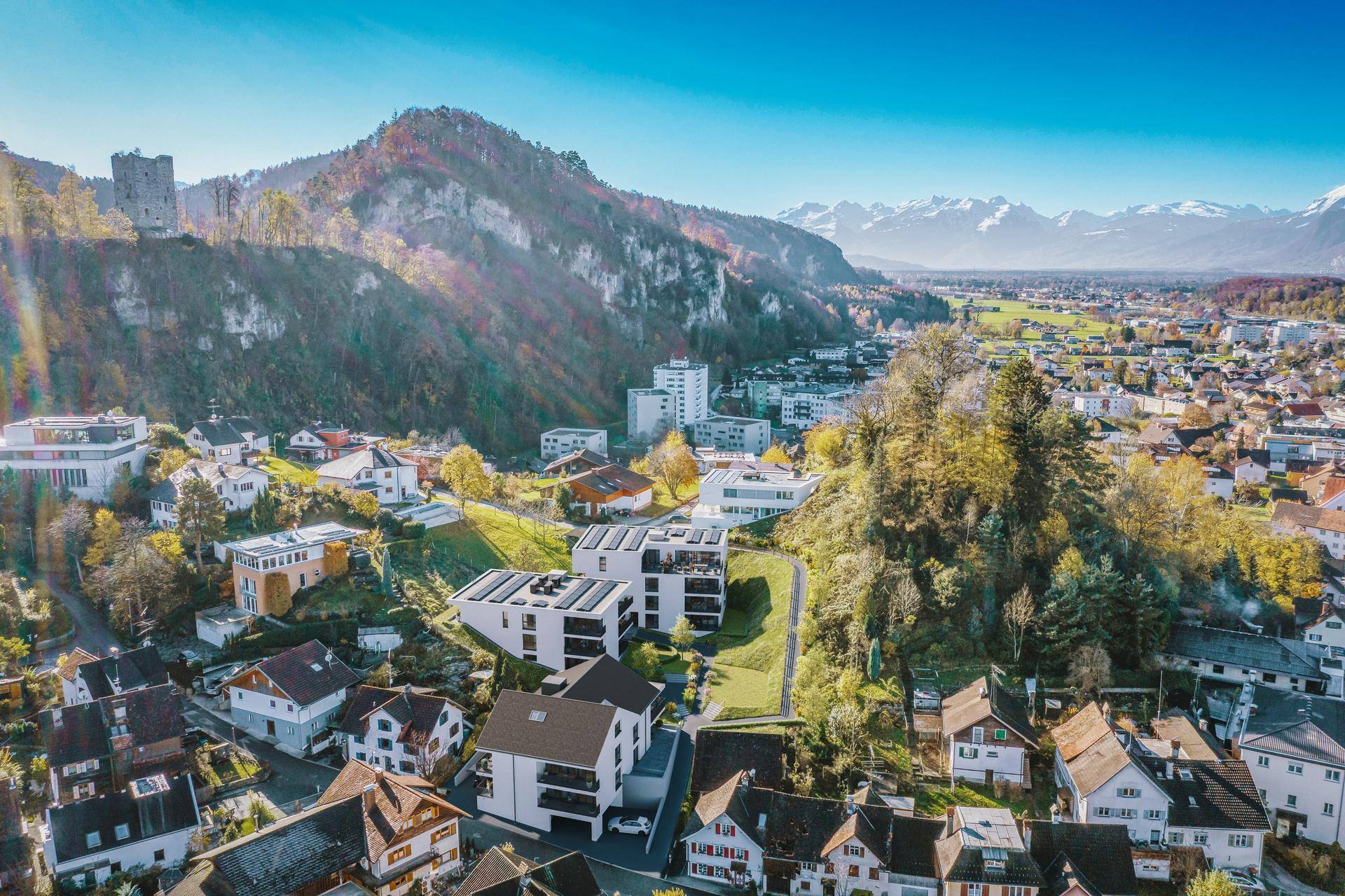 Luftaufnahme einer Wohnsiedlung mit Blick auf Berge und eine Burgruine.