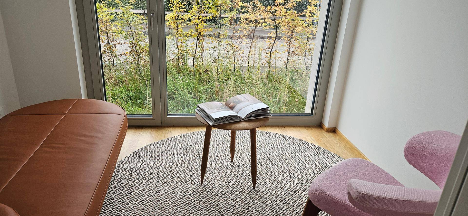 Gemütlicher Wohnbereich mit Ledersofa, Sessel und großem Fenster mit Blick auf die Natur.