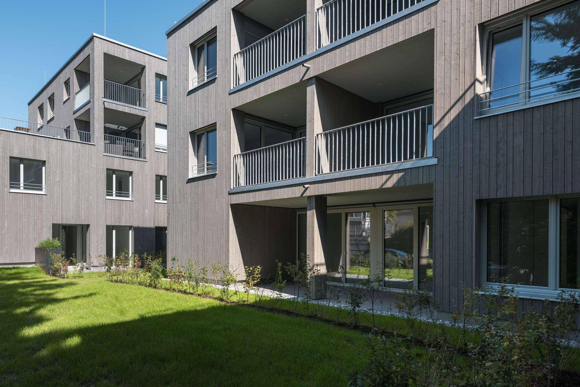 Ansicht des modernen Wohngebäudes mit mehreren Balkonen und einer grünen Rasenfläche.
