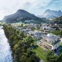 Eine malerische Luftaufnahme einer Stadt am Flussufer mit majestätischen Bergen im Hintergrund.