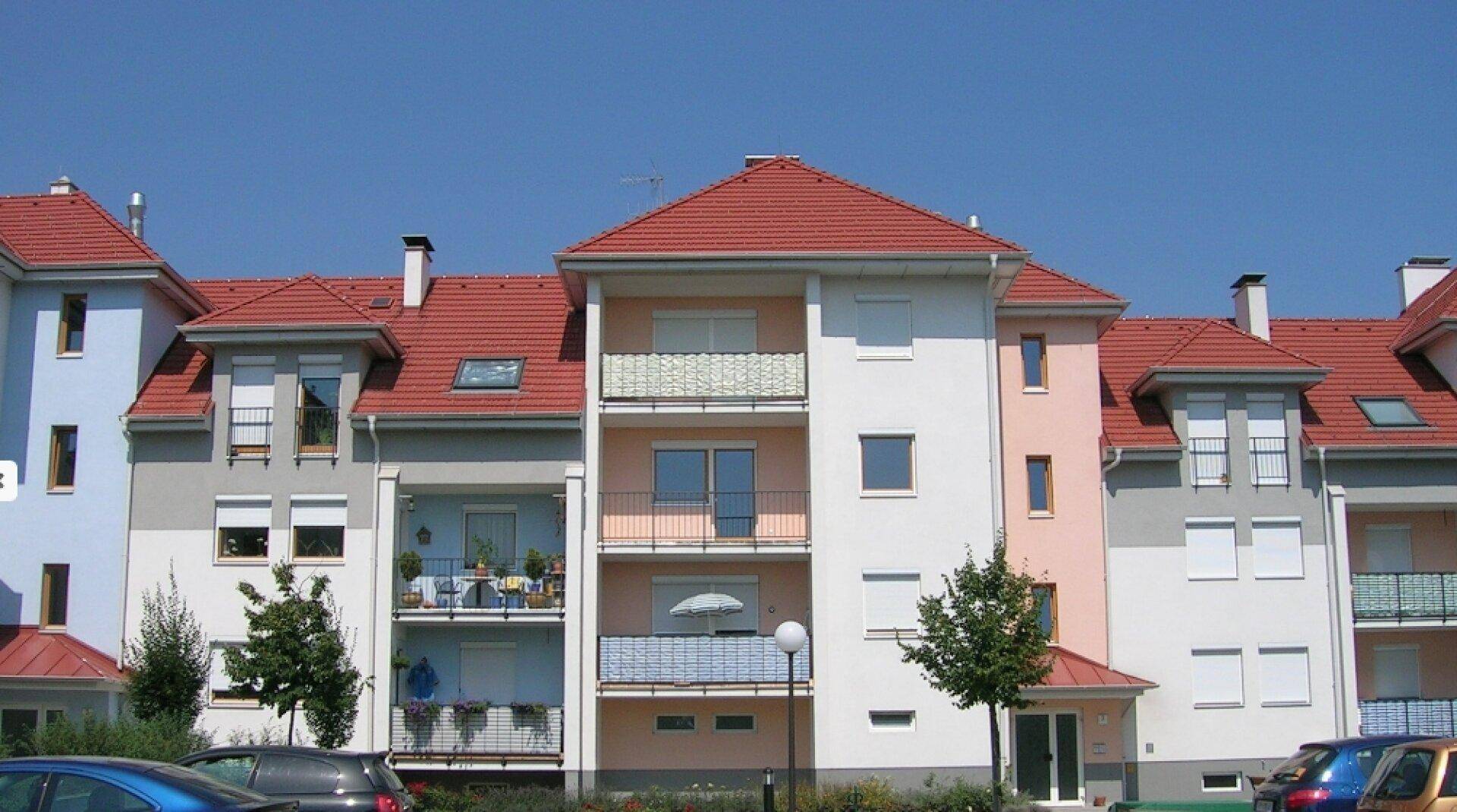 Moderne Wohnanlage mit farbigen Fassaden, roten Dächern und Balkonen unter blauem Himmel.